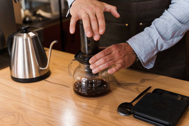 Aeropress coffee close-up: barista press to device and coffee drops pours trought aeropress to pot. Εναλλακτική μέθοδος παρασκευής σκανδιναβικού καφέ. - Φωτογραφία, εικόνα