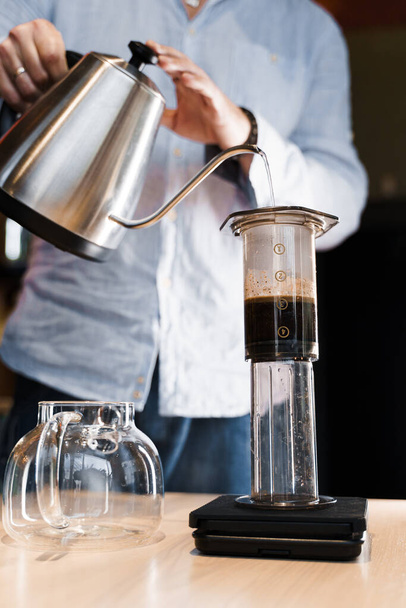 Aeropress kávé közeli alternatív barista a kávézó függőleges fotó. A Barista forró vizet öntött edénybe, hogy speciális eszközzel aeropress kávét készíthessen. Hirdetés kávézó, éttermek. - Fotó, kép