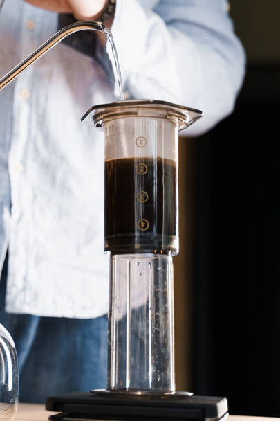 Aeropress Kaffee Nahaufnahme alternative Herstellung von Barista im Café vertikales Foto. Barista gießt heißes Wasser in Topf, um mit einem speziellen Gerät Aeropress-Kaffee herzustellen. Werbung für Cafés, Restaurants. - Foto, Bild