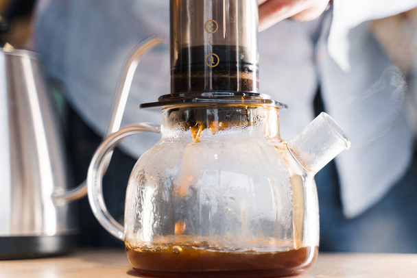 Aeropress coffee and glass pot close-up: barista press to device and coffee drops pours trought aeropress to pot. Alternative coffee brewing method. Barista makes coffee - 写真・画像