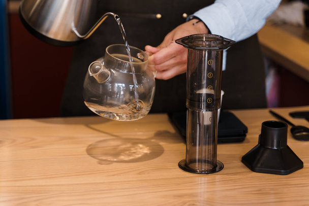 カフェでバリスタによるエアロプレスコーヒーの代替製造。バリスタは特別な装置との航空宇宙コーヒーを作るための鍋にお湯を注ぐ。カフェ、レストランの広告. - 写真・画像