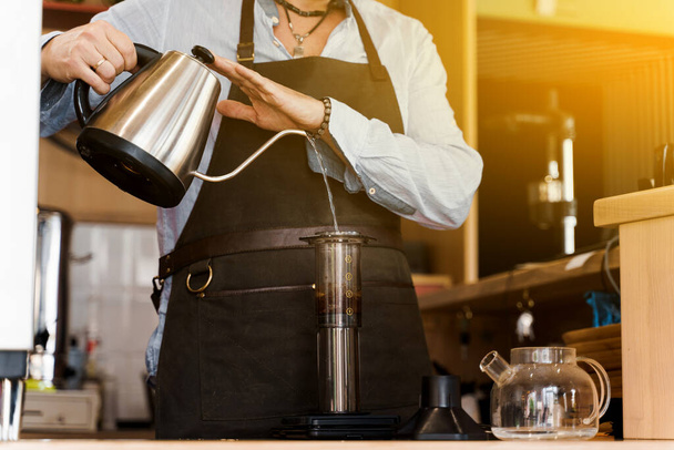 Aeropress koffie met zonlicht. Alternatief maken door barista in het café. Barista houdt kattle vast en giet water in aeropress met koffie. Scandinavische koffiezetmethode. - Foto, afbeelding