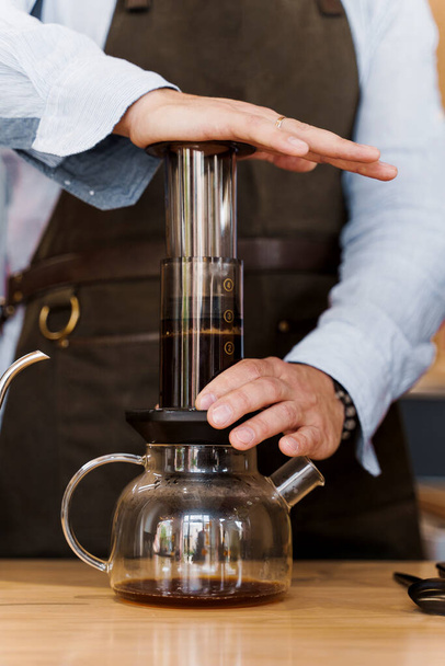 Aeropress koffie close-up: barista druk op apparaat en koffie druppels giet trought aeropress aan pot. Alternatieve koffiezetmethode. Verticale foto - Foto, afbeelding