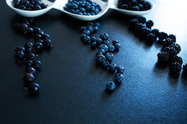 Set of different types of black berries in a white plate on a black table. Stylish seasonal vitamins. - Foto, Bild