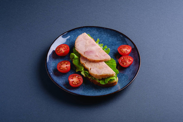 Sandwich met kalkoenham vlees, groene salade en verse kerstomaten plakjes op blauwe glanzende plaat, blauwe minimale achtergrond, hoek uitzicht - Foto, afbeelding
