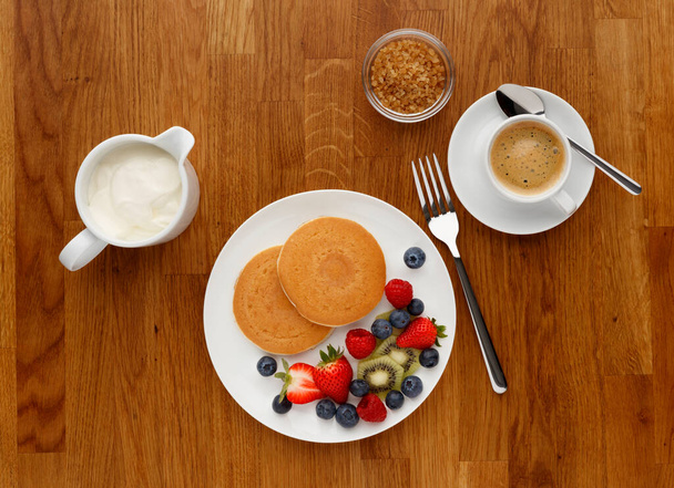 Kontinentales Frühstück mit Pfannkuchen, Obst und Kaffee, aufgenommen auf einer hölzernen Arbeitsplatte, von oben. - Foto, Bild