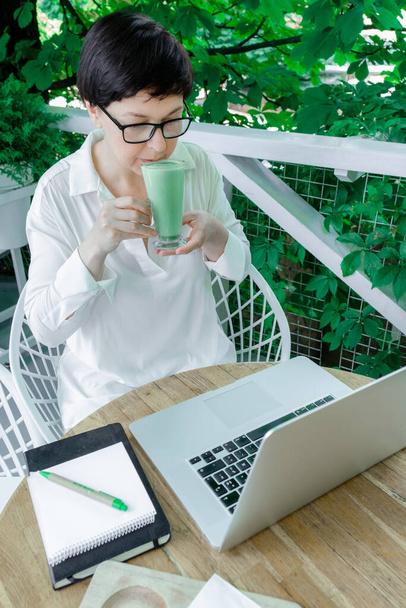 Kobieta Freelancer lub Blogger siedzi w miejscu pracy z filiżanką zielonej Matcha późnej kawy lub herbaty. Pojęcie zdrowej żywności w okresie menopauzy. - Zdjęcie, obraz