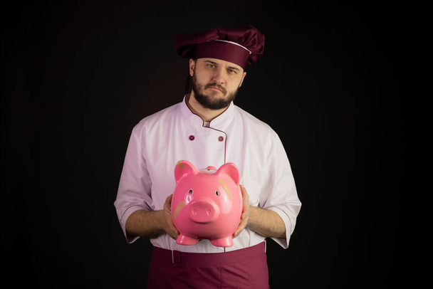 Sad chef man in uniform holds broken pink piggy bank with band-aid crisis - Photo, Image
