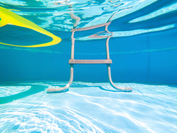 Grijze zwembadladder en gele luchtmatras gezien vanaf onderwater - Foto, afbeelding