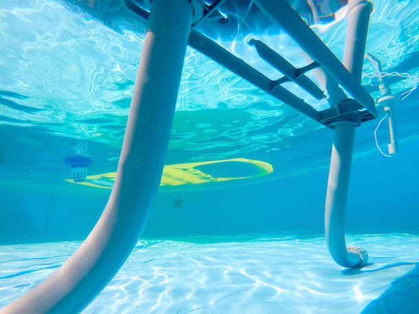 Escada de piscina vista debaixo d 'água com colchão de ar e dispensador de cloro no fundo
 - Foto, Imagem