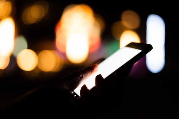 γυναίκα κρατά ένα κινητό τηλέφωνο με λευκή οθόνη τη νύχτα - Φωτογραφία, εικόνα