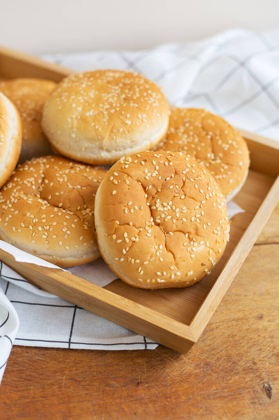 Freshly baked lush burger buns lie on a wooden tray on a table with a white napkin. Top view, close-up. Yellow flavored pastries with white sesame seeds - Φωτογραφία, εικόνα