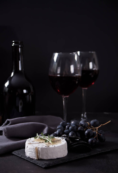 Two glass of red wine and plate with assorted cheese, fruit and other snacks for party. - Zdjęcie, obraz