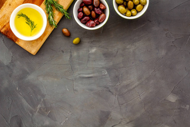 Olives and olive oil in bowls on cutting board on grey top view copy space - Foto, immagini