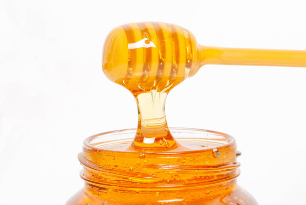 golden bee honey in a glass jar and honey dipper - Fotoğraf, Görsel