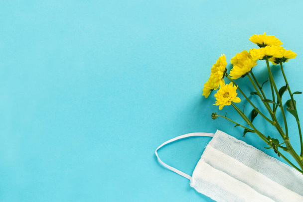 Seasonal spring summer allergy flowers concept. Yellow flowers with medical protective mask on blue background. Creative flat lay composition, copy space, minimal style - Foto, Bild