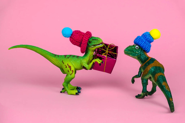 cute green toy dinosaur in knitted hat give present box to another dinosaur in hat, festive funny greeting card - Foto, Imagen