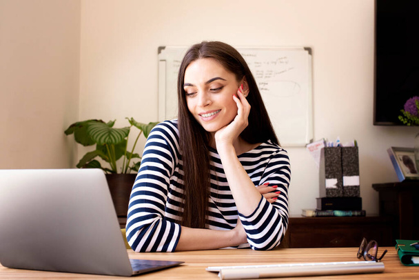 Shot of happy businesswoman talking to her colleagues about business plan in video conference while sitting behind her laptop at home. Home office.  - Foto, immagini