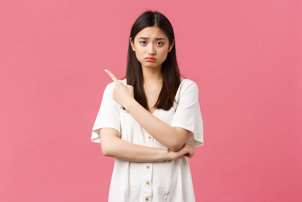 Beauty, people emotions and summer leisure concept. Upset gloomy girl in white dress, sulking and frowning as pointing upper left corner at bad news, disappointing advertisement banner - Photo, Image