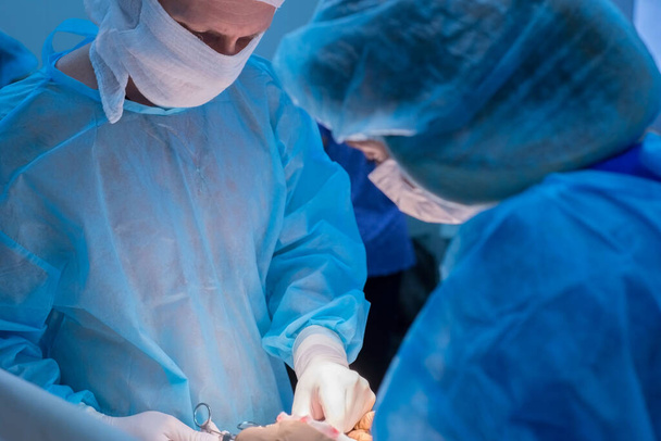 Children's surgeons perform urological operations. A man and a woman in a mask and a blue sterile coat in the operating room. A team of surgeons is conducting an operation. Treatment of inguinal hernia, testicular edema, testicular disease, varicocel - Photo, Image