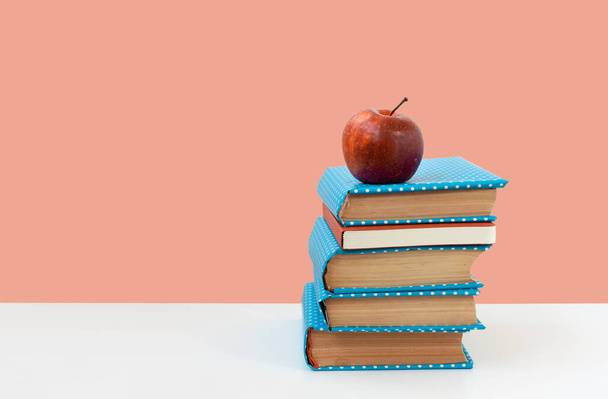 Powrót do szkoły, stos książek i czerwone jabłko na białym stole z różowym tłem. Wykształcenie na odległość. Koncepcja kwarantanny w domu - Zdjęcie, obraz