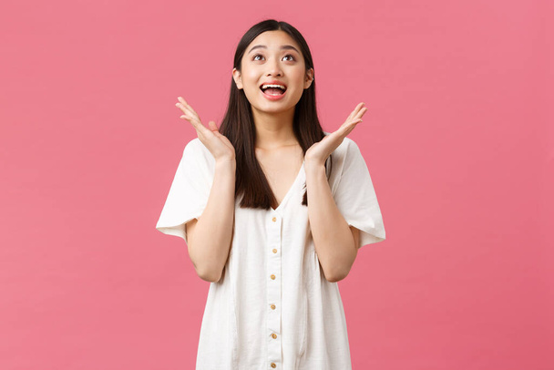 Beauty, people emotions and summer leisure concept. Happy cheerful asian girl clap hands and smiling upbeat, looking up with amazed face, enjoying performance, applause over pink background - Фото, зображення