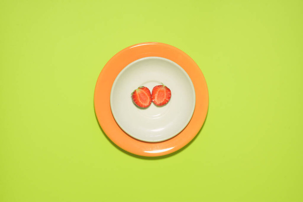 Minimal strawberry slice background. Fruit on white and orange colored plate with leaves around it. - Foto, afbeelding