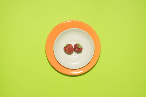 Ελάχιστο φόντο φράουλας. Φρούτα σε λευκό και πορτοκαλί χρώμα πιάτο με φύλλα γύρω από αυτό. - Φωτογραφία, εικόνα