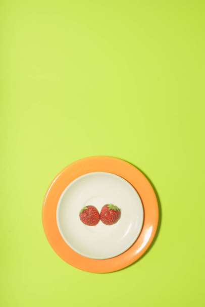 Rebanada de fresa en plato blanco y naranja sobre fondo de color verde lima. Diseño vertical para un folleto, pancarta, portada o folleto
 - Foto, Imagen