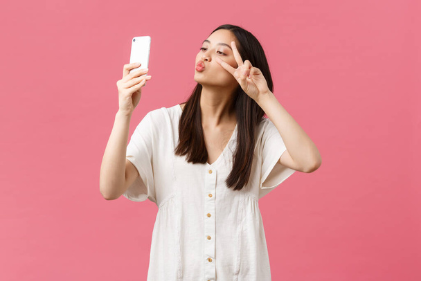 Ομορφιά, ανθρώπινα συναισθήματα και τεχνολογική αντίληψη. Γυναίκα όμορφη κομψή ασιατική blogger κορίτσι λήψη selfie στην κάμερα smartphone, χαμογελώντας χαρούμενος στο κινητό τηλέφωνο, στέκεται ροζ φόντο - Φωτογραφία, εικόνα