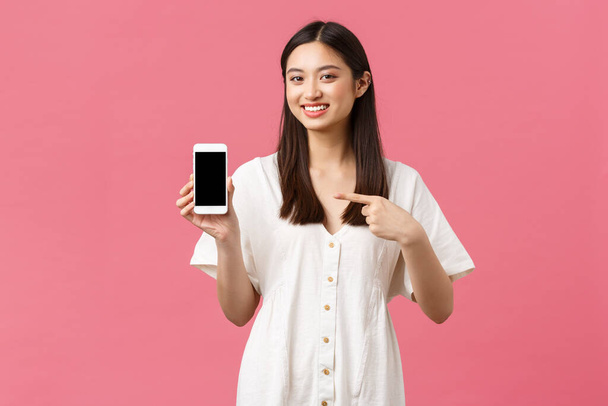 Beleza, emoções das pessoas e conceito de tecnologia. Menina coreana muito elegante mostrando aplicativo na tela do smartphone. Mulher promovendo loja ou aplicativo, apontando o dedo para o telefone celular e sorrindo
 - Foto, Imagem