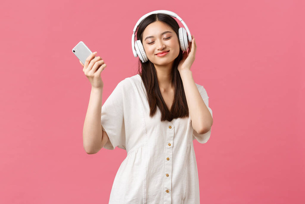 Krása, emoce lidí a technologický koncept. Carefree a hezká asijská dívka těší hudbu v bezdrátových sluchátkách, zavřít oči a usměvavý poslech oblíbené písně, držení smartphone a tanec - Fotografie, Obrázek