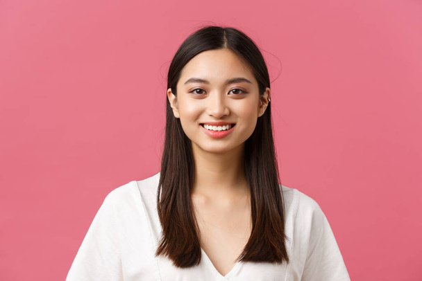 Beauty products advertisement, haircare and women fashion concept. Close-up of cute romantic silly asian girl with medium dark haircut, smiling white teeth with happy expression, pink background - 写真・画像