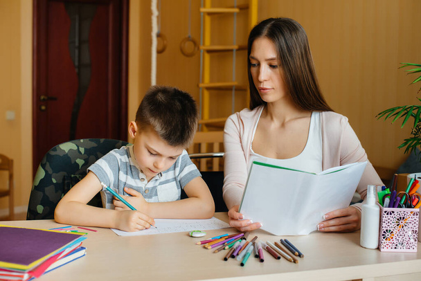 A young mother is doing homework with her son at home. Parents and training - Foto, imagen