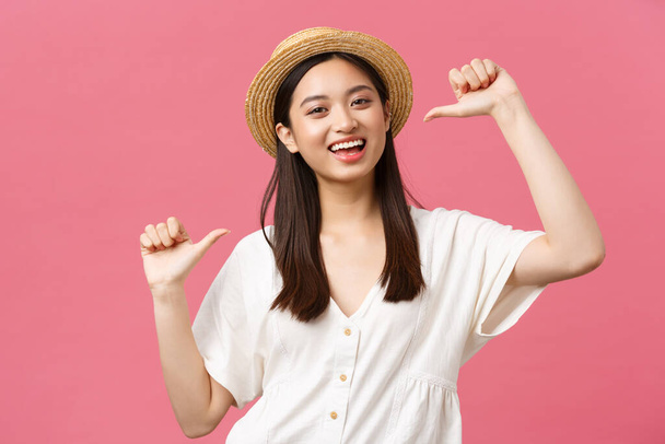 Kauneus, ihmiset tunteita ja kesän vapaa-ajan ja loma käsite. Lähikuva onnellinen innostunut nainen Aasian turisti olki hattu osoittaa itseään ja hymyillen, kehuskelevat vaaleanpunainen tausta - Valokuva, kuva
