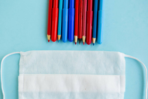 Color pencils and medical mask on blue background, top view, back to school concept, school quarantine concept - Fotó, kép