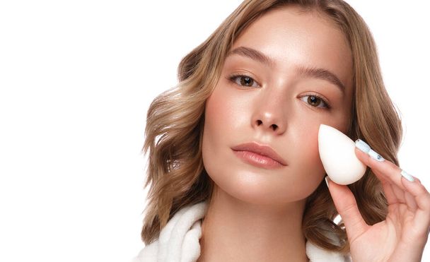 Beautiful tender young girl in a white coat with clean fresh skin posing in front of the camera with a sponge in her hands. Beauty face. Skin care. - Foto, Bild