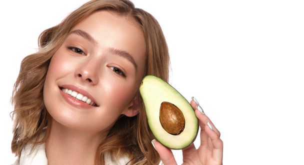 Beautiful tender young girl in a white coat with clean fresh skin posing in front of the camera with avocado in her hands. Beauty face. Skin care. - Φωτογραφία, εικόνα