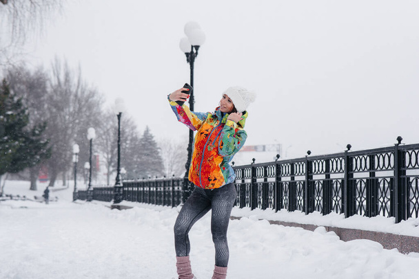 A young athletic girl takes a selfie on a frosty and snowy day. Fitness, recreation - Фото, изображение