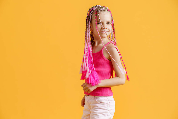 Stylish girl with pink dreadlocks and posing on a yellow background. Beauty, fashion. - Photo, Image