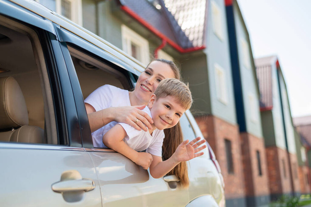 Happy woman and child look out of a car window. Cheerful boy with his mother are sitting in the back seat of the car and ready for the journey. Summer vacation concept. Family road trip. - Φωτογραφία, εικόνα