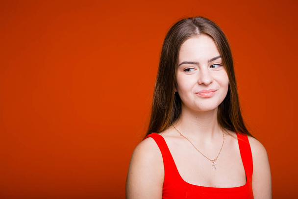 Emotional portrait of a European girl with long hair who playfully looks away on an orange background - Photo, Image