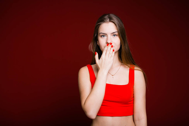 Italian girl looking at the camera and covering her mouth with her hand as a sign of silence and keeping secrets on a burgundy background - Фото, изображение