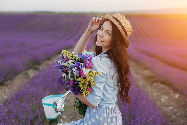 pretty brunette woman running away in lavender field. woman in dress and straw hat having fun in flowers of lavender - Fotoğraf, Görsel