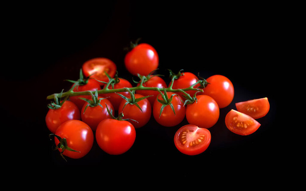 Pomidory wiśniowe świeże i dojrzałe obok krojonych pomidorów na czarnym tle izolowane. Ingridient do sałatki warzywnej lub ketchupu. Wegetariańskie odżywianie ekologiczne - Zdjęcie, obraz