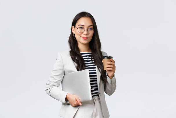 Biznes, finanse i zatrudnienie, koncepcja odnoszących sukcesy kobiet przedsiębiorców. Pewna siebie, dobrze wyglądająca bizneswoman w okularach i garniturze pijąca kawę na wynos i niosąca służbowego laptopa - Zdjęcie, obraz