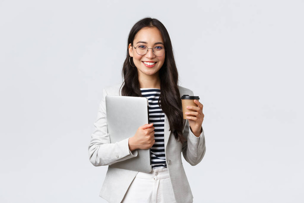 Business, finance and employment, female successful entrepreneurs concept. Confident good-looking businesswoman in glasses and suit drinking takeaway coffee and carry work laptop - Photo, Image