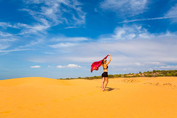 Hermosa chica caucásica divirtiéndose en las dunas de arena roja en Mui Ne, área de Phan Tiet en Vietnam. Paisaje con cielo azul durante el día soleado
. - Foto, Imagen