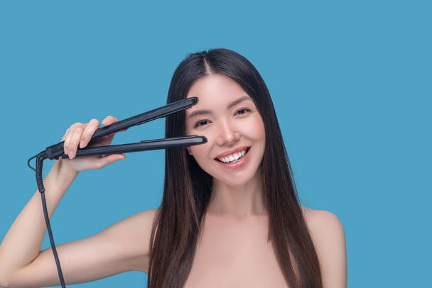 Smiling long-haired woman holding a straightening iron - 写真・画像