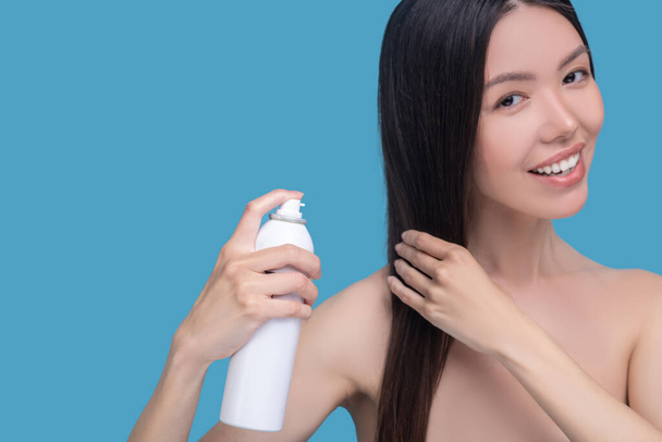 Smiling woman spraying new hairspray on her hair - 写真・画像